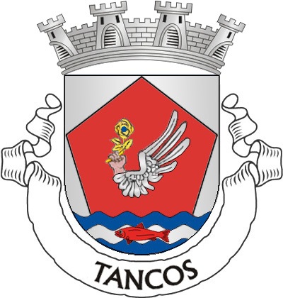 Escudo de prata, com pentágono de vermelho firmado na linha superior do escudo e nos flancos, movente de um pé ondado de
três tiras, de prata e azul, com um sável nadando, de vermelho; o pentágono
carregado de uma mão de carnação, alada de prata e sustendo nos dedos uma rosa de ouro, folhada do mesmo, botoada de azul. Coroa mural de prata de quatro torres. Listel branco, com a legenda a negro:
“TANCOS”.