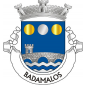 Escudo de azul, ponte de três arcos torreada à dextra, de prata, lavrada de negro, movente dos flancos e saínte de ponta ondada de prata e azul de três burelas; em chefe, besante de prata entre dois besantes e ouro. Coroa mural de prata de três torres. Listel branco, com a legenda a negro: "BADAMALOS". 