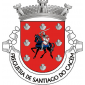 Escudo de vermelho, cavaleiro vestido de cota de malha de prata, brandindo na mão direita a espada do mesmo, sustendo no braço esquerdo escudo amendoado de prata carregado com a cruz da Ordem de Santiago e montado num corcel de negro, arreiado de azul; em orla, oito vieiras de prata. Coroa mural de prata de três torres. Listel branco com a legenda a negro: “FREGUESIA DE SANTIAGO DO CACÉM“. 