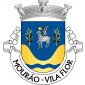 Escudo de azul, ?Agnus Dei? de prata, nimbado de ouro, sustendo com a mão direita uma haste crucífera de ouro, de onde pende um lábaro de prata, carregado de uma cruz firmada de vermelho, tudo entre dois ramos de oliveira de ouro, frutados de negro e postos em pala; em campanha, vale de ouro carregado de uma burela ondada de azul. Coroa mural de prata de três torres. Listel branco, com a legenda a negro: ?MOURÃO -VILA FLOR?.